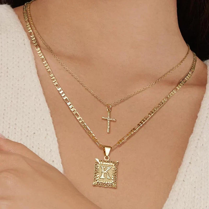 Close-up of the layered cross and square K pendant necklaces worn against a cream knit sweater 8