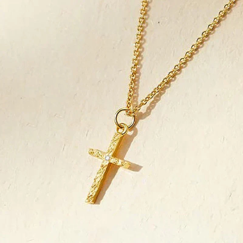 Close-up of the gold cross pendant on a fine chain, showing its hammered texture and tiny stone 4