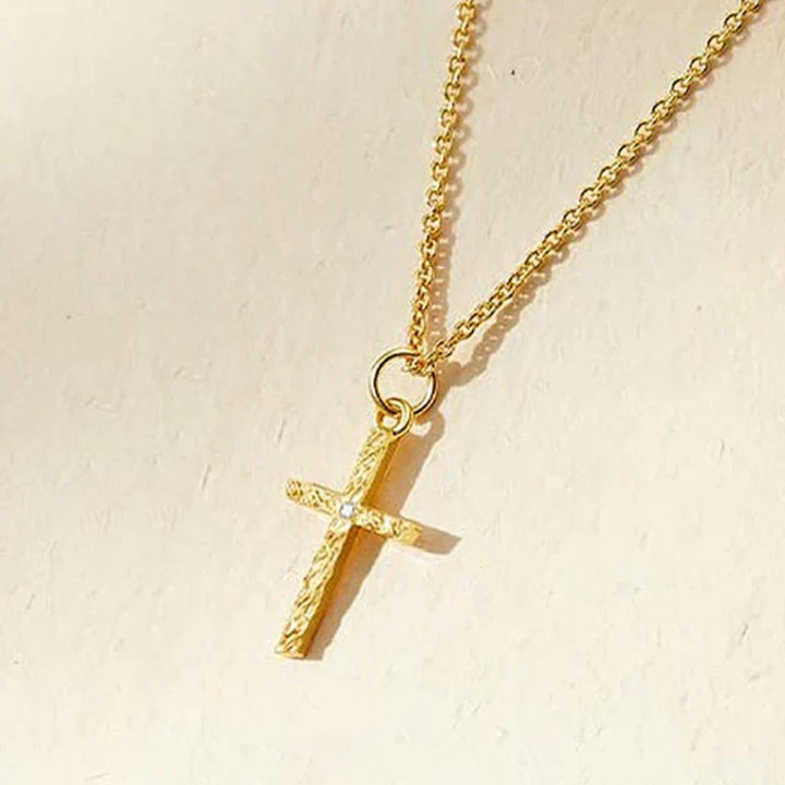 Close-up of the gold cross pendant on a fine chain, showing its hammered texture and tiny stone 4
