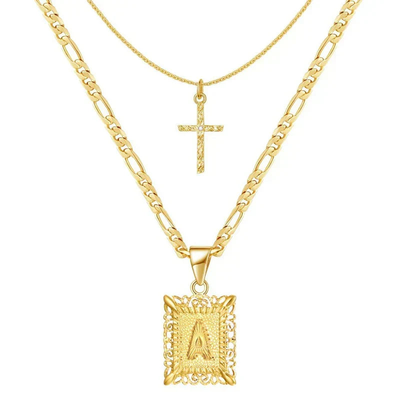 Two layered gold chains on white, a small textured cross and an ornate square letter pendant 1
