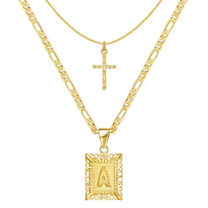 Two layered gold chains on white, a small textured cross and an ornate square letter pendant 1