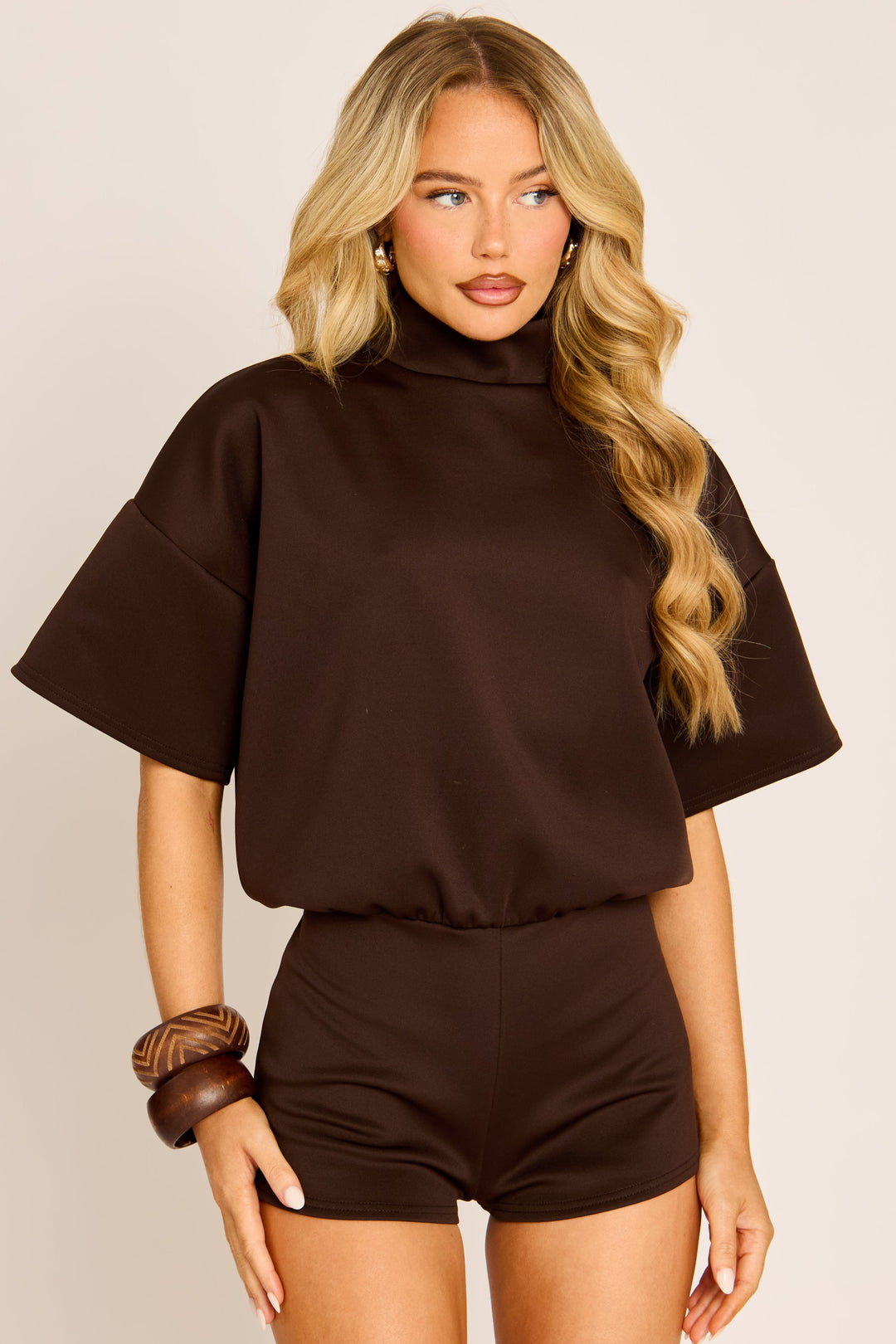 Close three-quarter front view of the brown playsuit on a model, showing the high neck and wide short sleeves 1