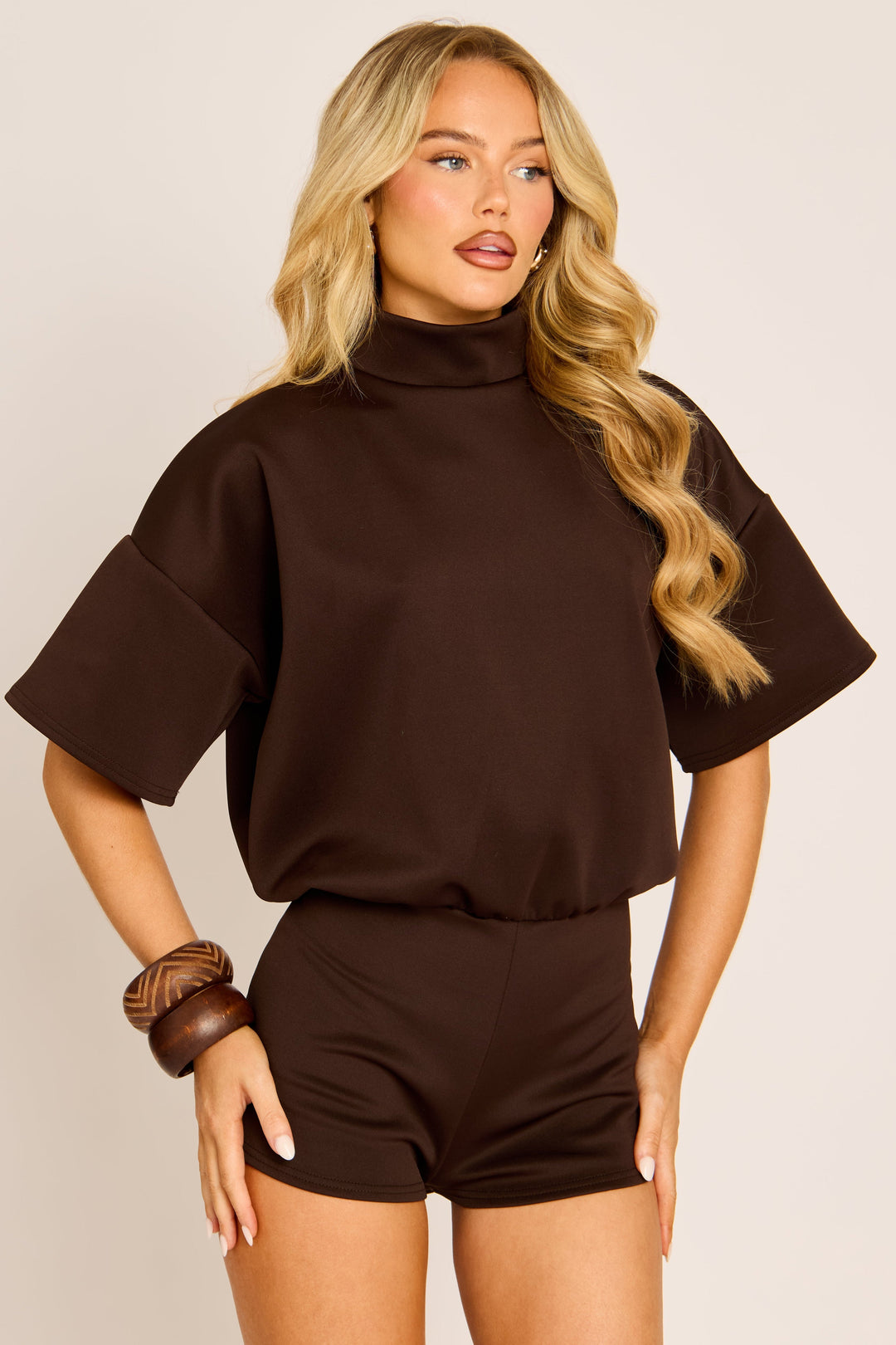Model with hands on hips in the brown playsuit, showing the oversized sleeves and fitted shorts 3