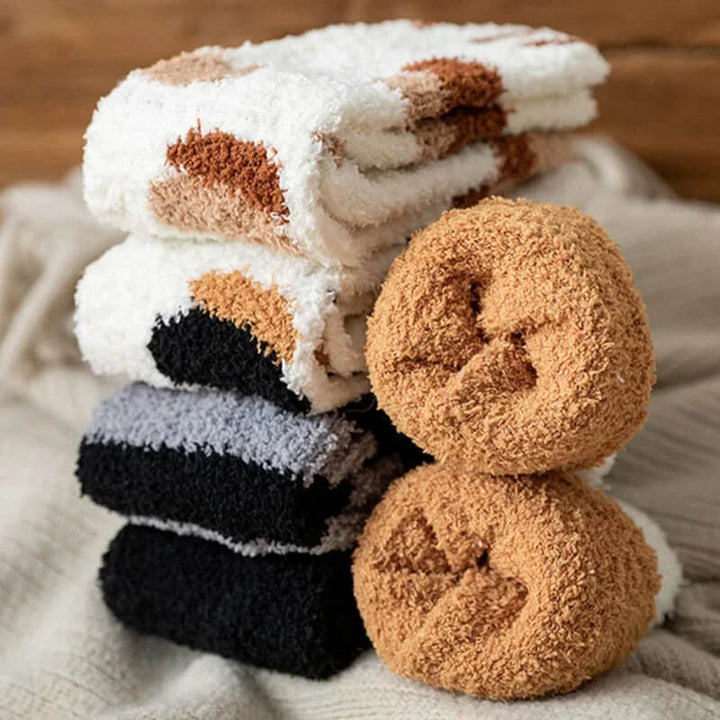 Stack of folded calico, black and striped fuzzy socks beside two tan pairs rolled into balls 4