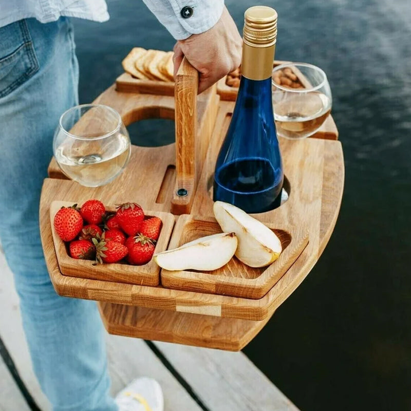 Man carrying the loaded wooden table by its handle on a dock, with wine glasses, strawberries, pear slices, and a bottle 5