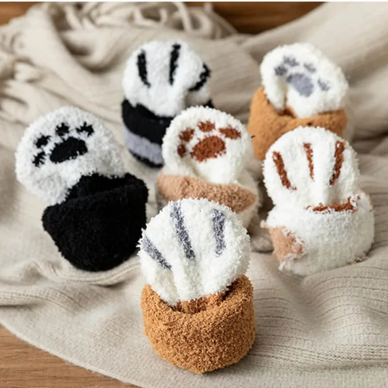 Six pairs of fluffy socks rolled up with the paw-print toe side facing up on a knit blanket 1