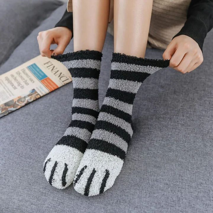 Model stretching black and gray striped fuzzy socks with white paw toes while sitting on a gray couch 10