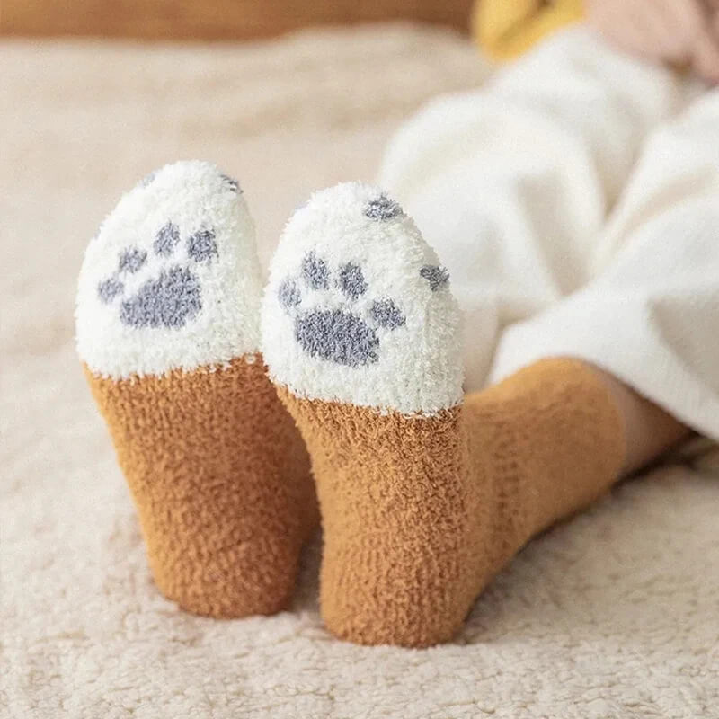 Back view of a person lying down wearing tan fuzzy socks with gray paw prints on the soles 3
