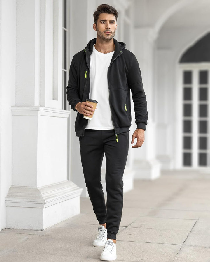 Man walking outdoors holding a coffee, wearing the black tracksuit with the jacket open over a white tee 25