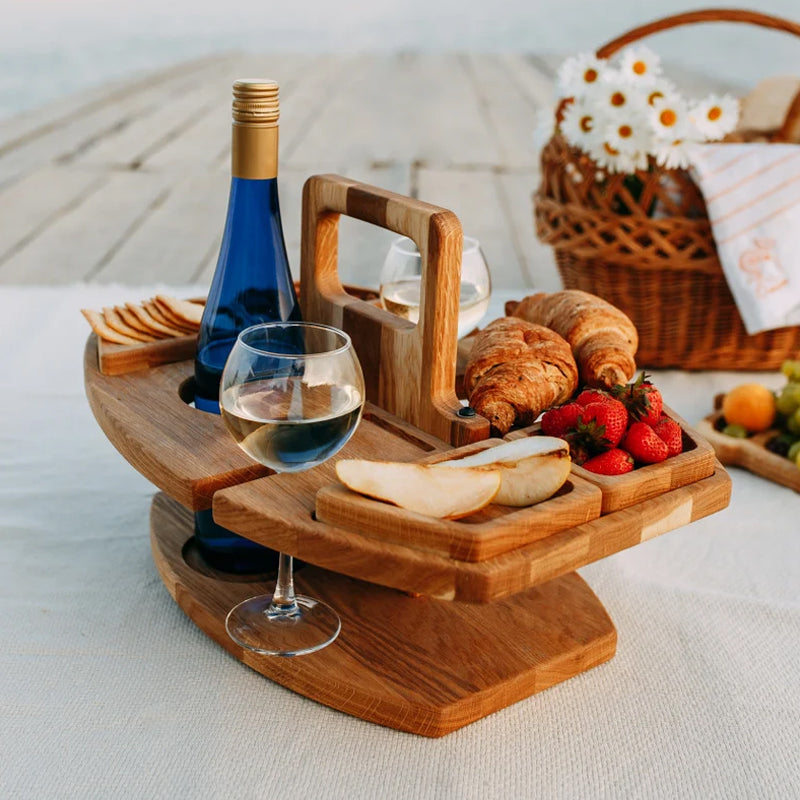 Wooden snack table set outdoors on a picnic blanket with croissants, strawberries, pear slices, wine and a wicker basket 2