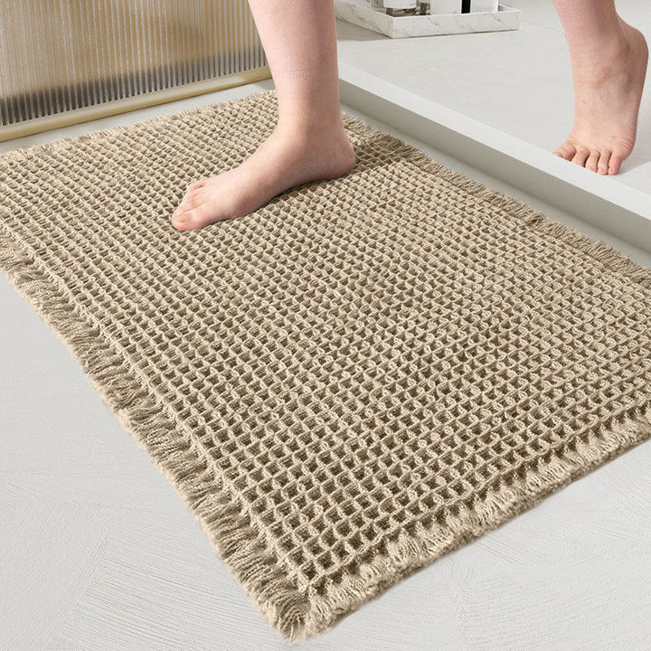 Close-up of the beige waffle-weave mat with fringed edges and a bare foot stepping on it 8