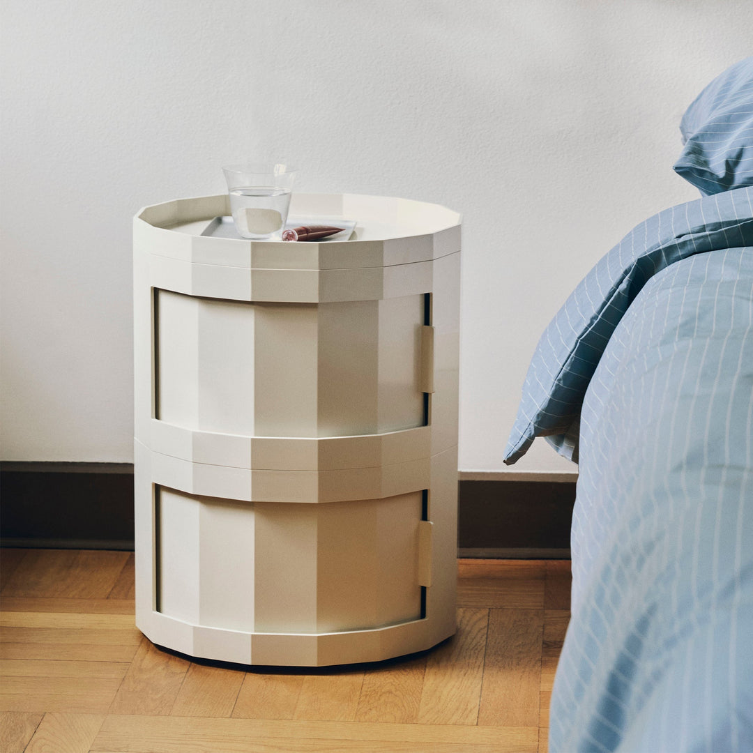 Two-tier cream cabinet used as a bedside table, holding a glass of water, next to a bed 52