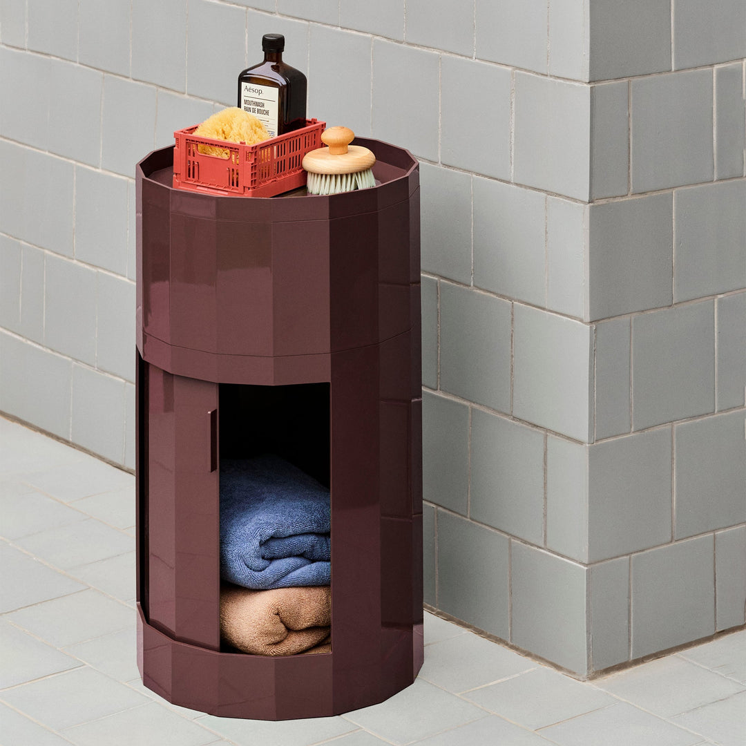 Burgundy cabinet in a tiled bathroom, door open showing folded towels, with bath items on top 47