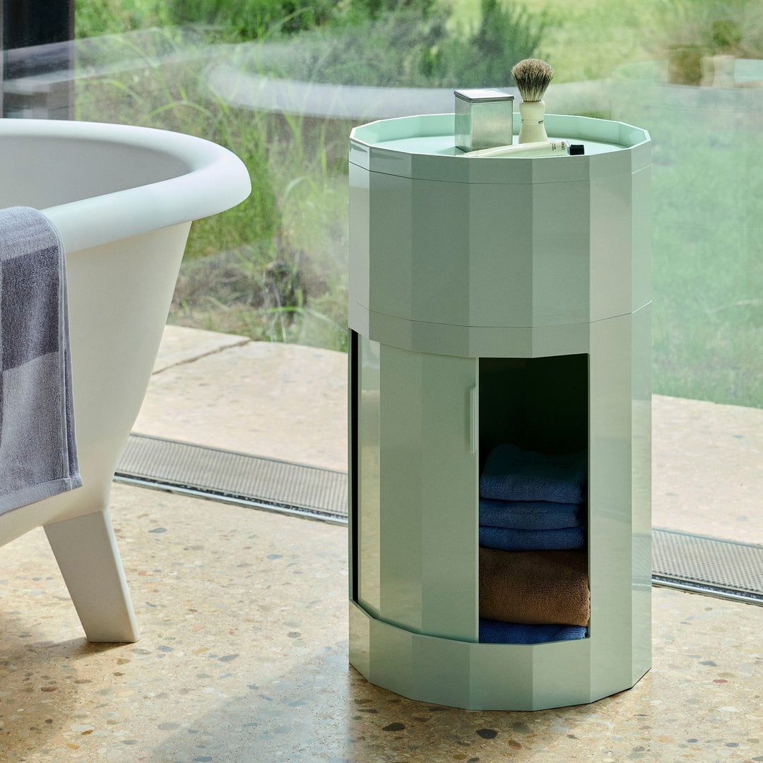 Mint green cabinet beside a bathtub, door open showing stacked towels, with shaving items on top 48