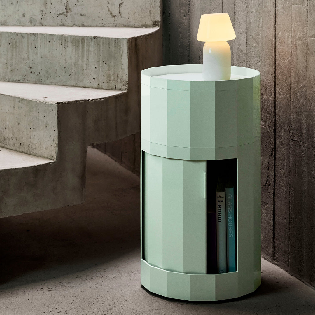 Mint green tall round cabinet beside concrete stairs, door open with books and a glowing lamp on top 18