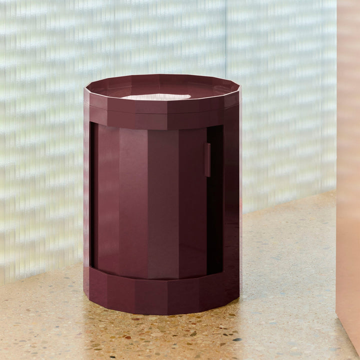 Burgundy single-tier cabinet with closed swivel door on a terrazzo surface in front of ribbed glass 49