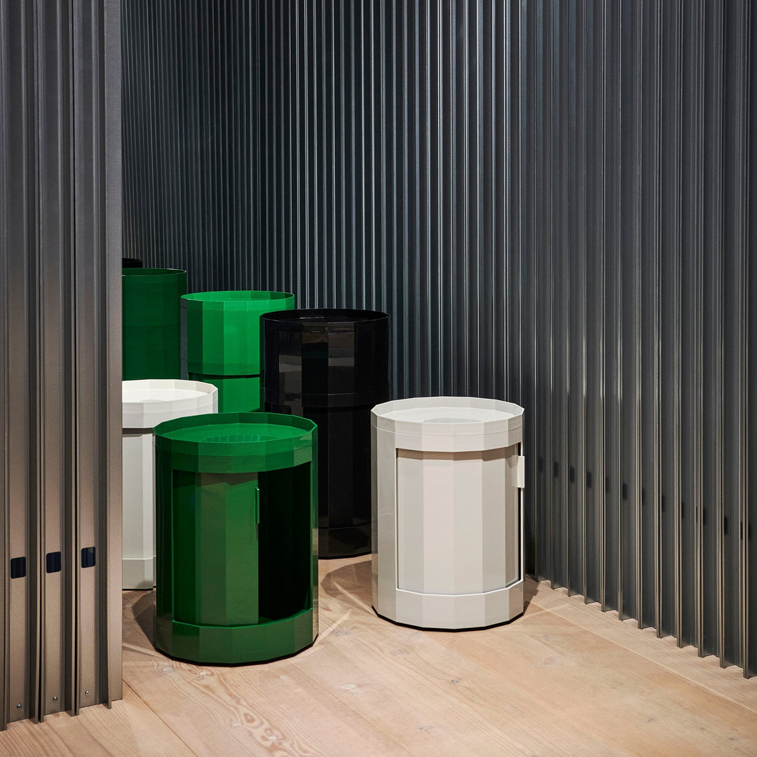 Showroom grouping of green, black, white and gray round cabinets of different heights against a ribbed dark wall 9