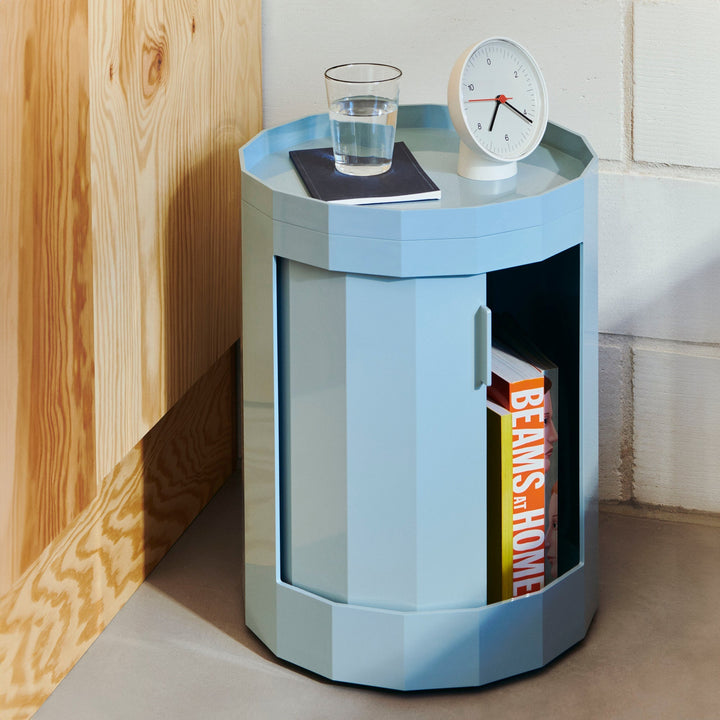 Light blue short round cabinet used as a nightstand, door open with books, glass and clock on top 11
