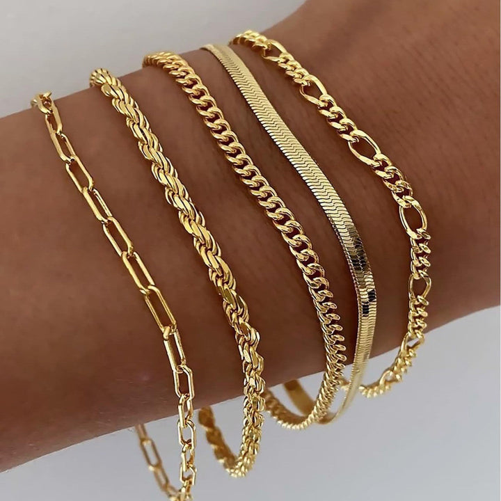 Five gold chain bracelets in varied link styles stacked together on a wrist 2