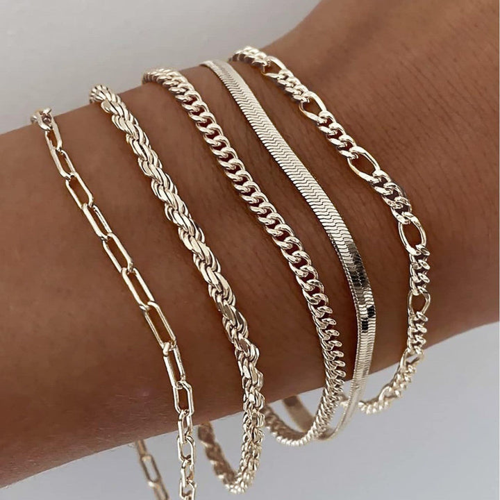 Five pale champagne gold chain bracelets in different link styles layered on a wrist 3