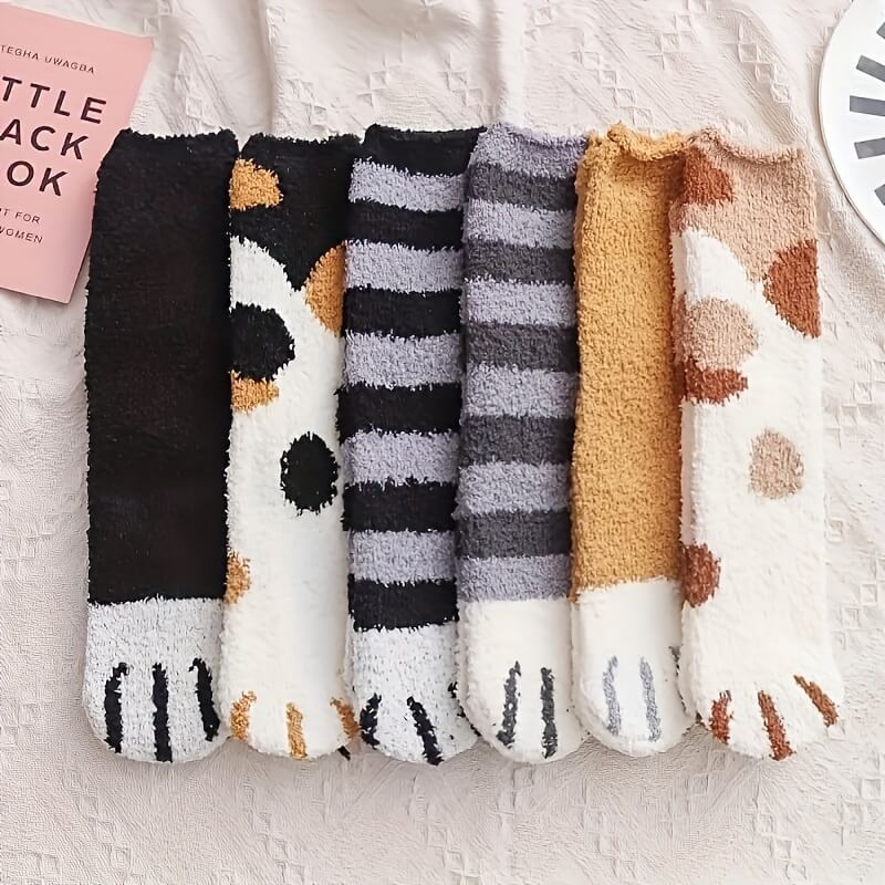 Six fuzzy socks laid side by side on a cream cloth, showing black, calico, striped and tan designs 2