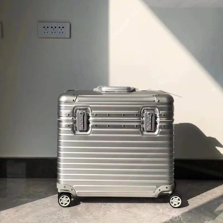 Front view of a silver grooved suitcase with two combination locks, standing near a sunlit wall 8