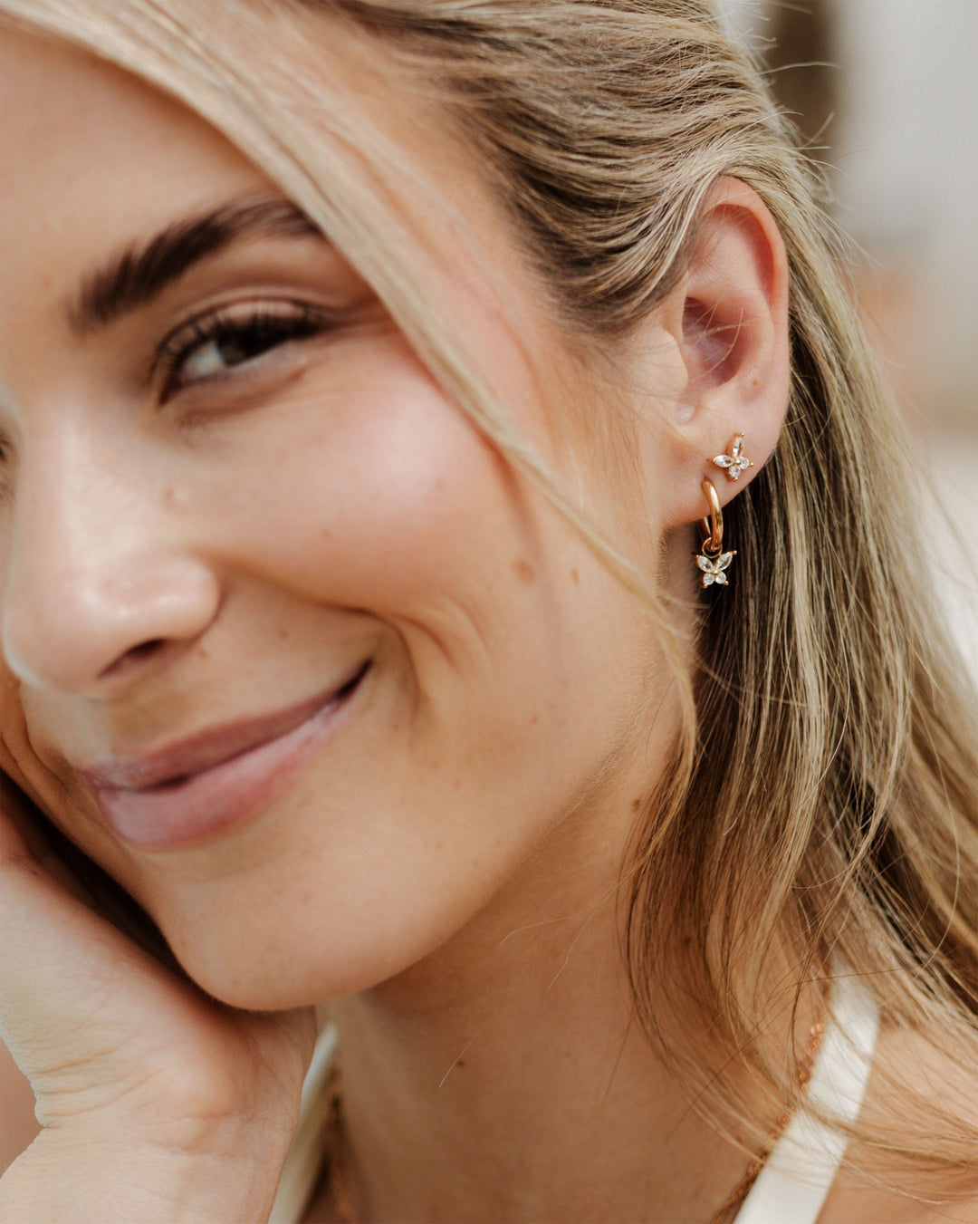 Smiling woman wearing rose gold-tone butterfly studs, one in the upper ear and one as a hoop charm 8