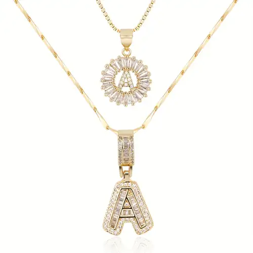 Two gold layered necklaces on white, one with a sparkling round initial pendant, one with a block letter 1