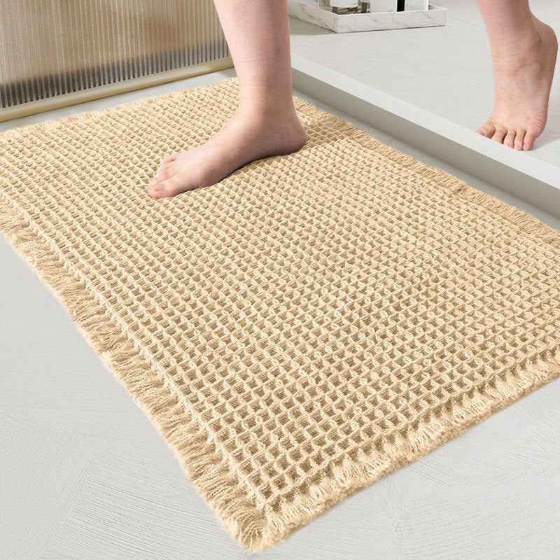 Close-up of the waffle-weave mat in light sand with fringed edges and a bare foot on it 13
