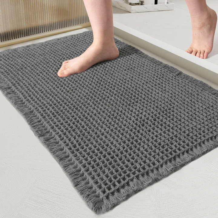 Close-up of the waffle-weave mat in charcoal gray with fringed edges and a bare foot on it 12