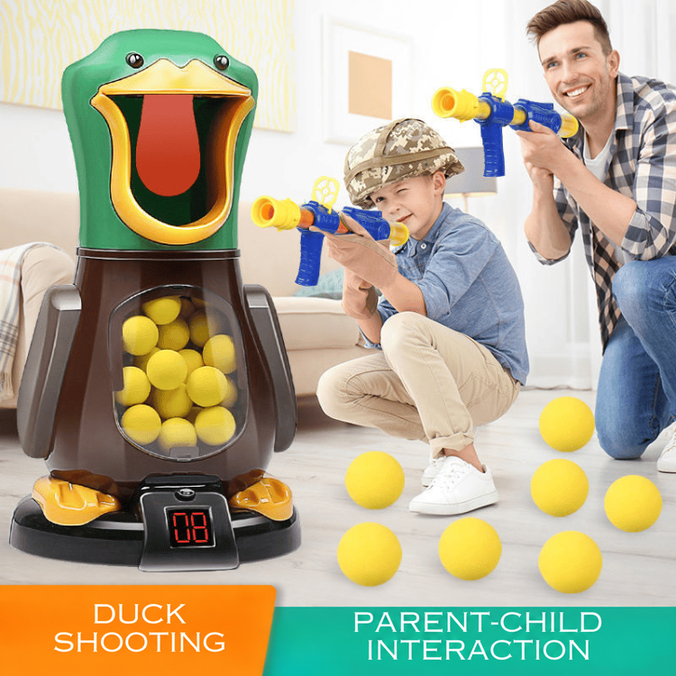 A father and son crouch with blasters aiming at the green duck target, yellow foam balls scattered nearby 2