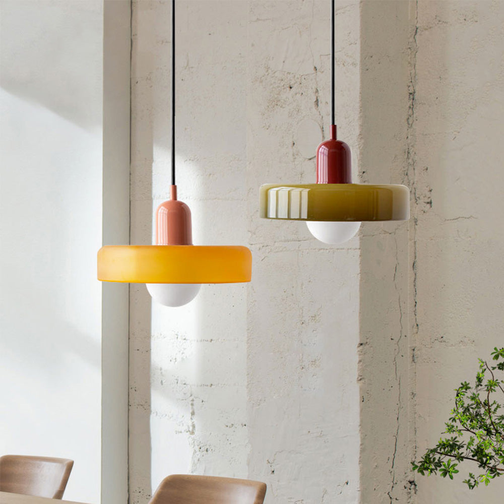 Two disc-shaped glass pendants, one amber and one olive, hanging by a rough white wall 1