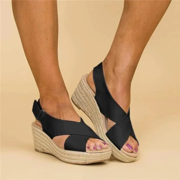 Black crisscross-strap wedge sandals with adjustable ankle straps, worn against a beige backdrop 4