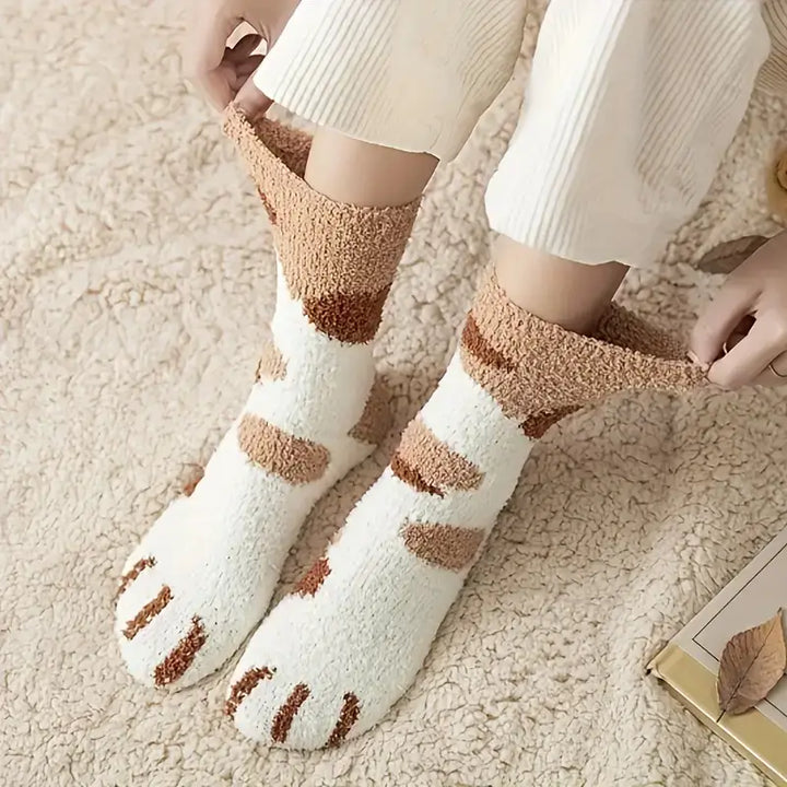 Model pulling up white fuzzy socks with brown spots and brown claw stripes on the toes, sitting on a shaggy rug 6