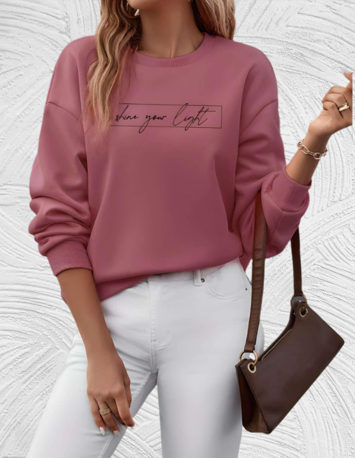 Frau in rosa Pullover mit Schriftzug, weiße Hose, braune Tasche, modisch, lässig.
