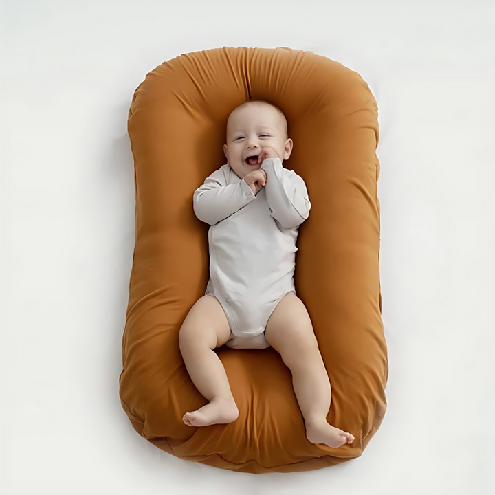 Overhead view of a giggling baby in a white bodysuit on a rust-orange lounger 3