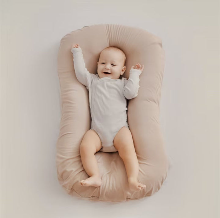 Overhead view of a smiling baby with raised arms on a beige lounger 7