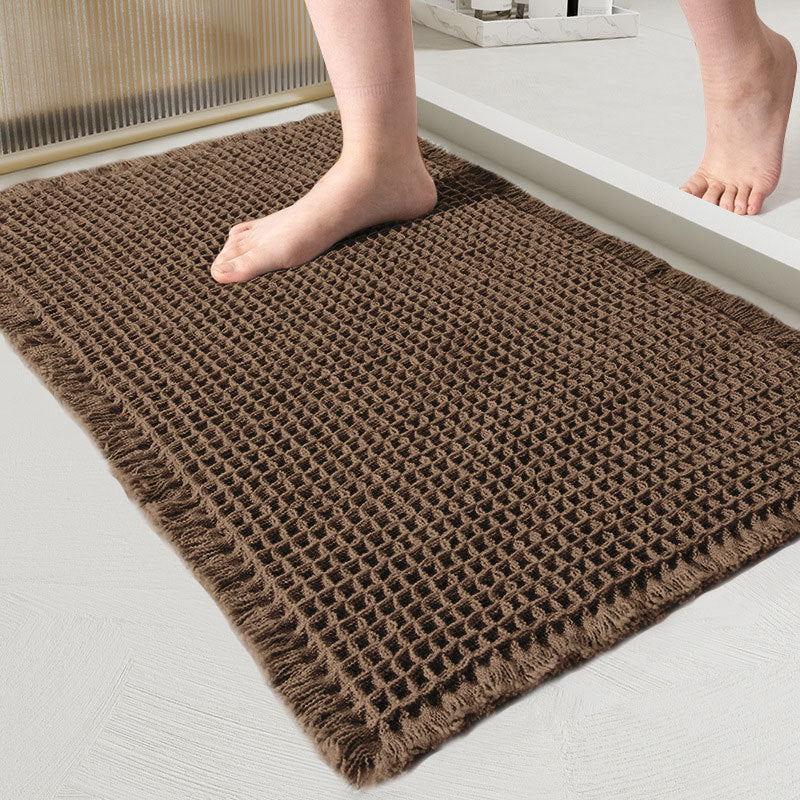 Close-up of the waffle-weave mat in dark brown with fringed edges and a bare foot on it 11