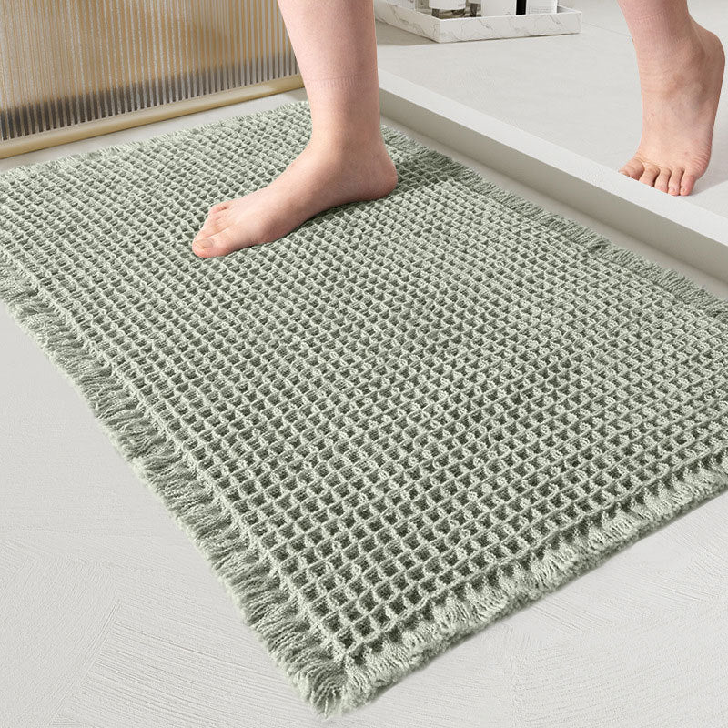 Close-up of the waffle-weave mat in sage green with fringed edges and a bare foot on it 9