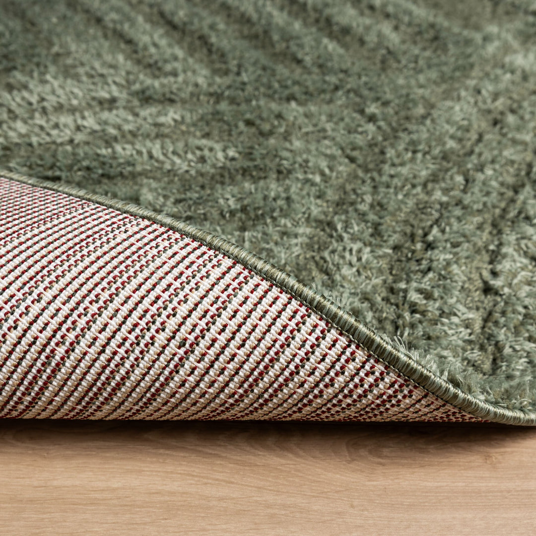 Rug corner folded over to show the woven white backing with colored dots beneath the green pile 7