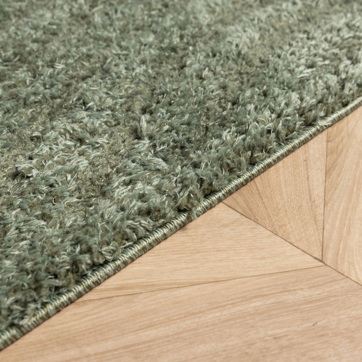 Angled close-up of the finished rug edge with its fluffy green pile beside the wood floor 6