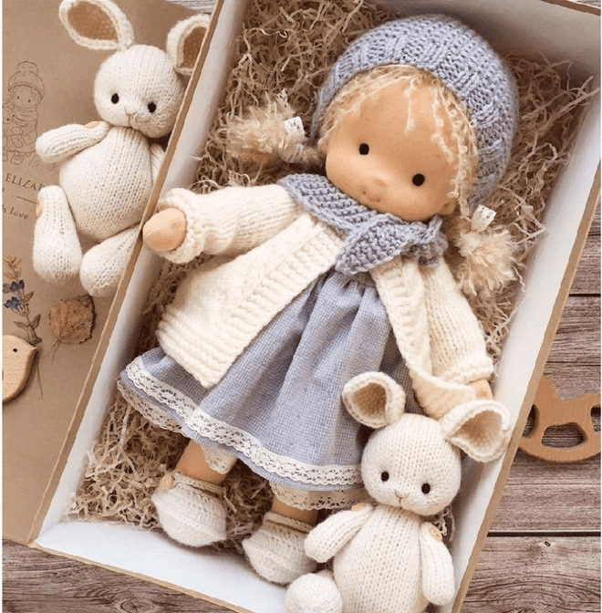 Doll in gray-blue knit bonnet and scarf, cream cardigan and gray dress with lace hem, between two knit bunnies 3