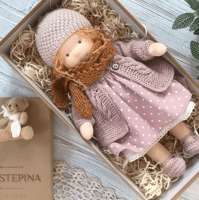 Doll with orange curls in a lilac knit hat, polka-dot dress and rust scarf, lying in a gift box 5