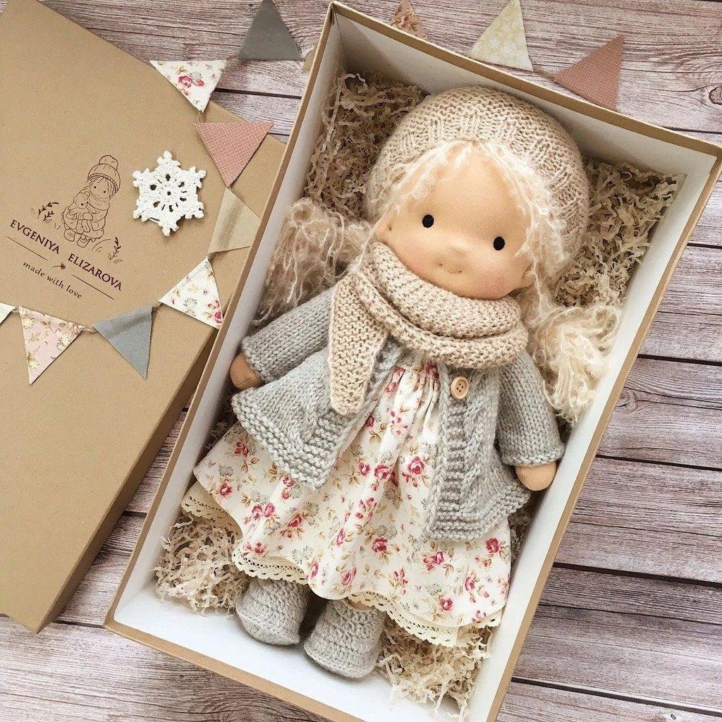 Doll with long blonde curls in beige knit hat and scarf, gray cardigan and floral dress, in a gift box 6