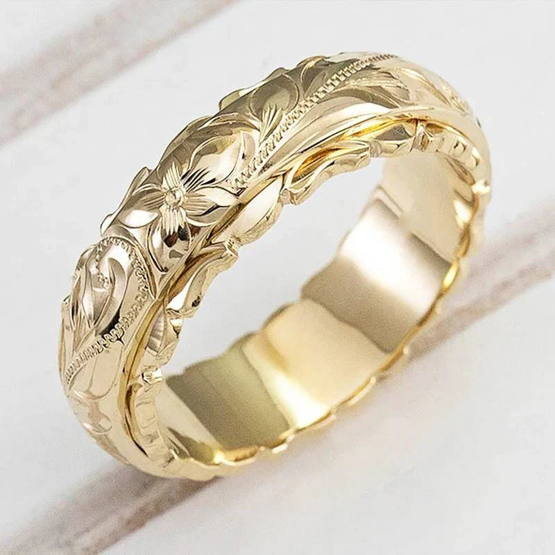 Close-up of a gold-toned band with engraved flowers and scrolling leaves, resting on a white wooden surface 1