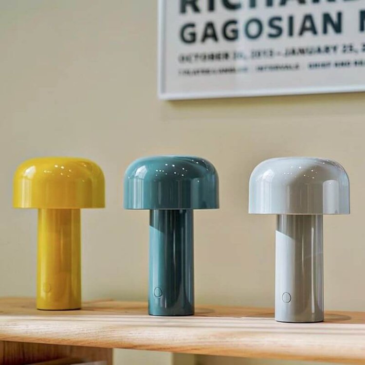 Yellow, teal and light gray lamps lined up on a wooden shelf below a framed poster 11
