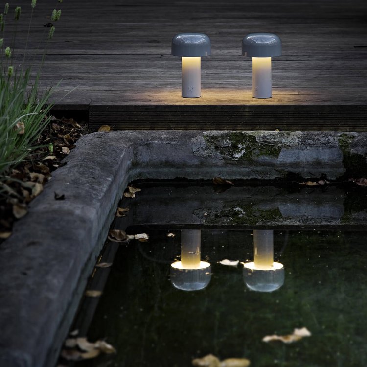 Two lit lamps on a dark wooden deck, their glow reflected in the water of a stone pool 13
