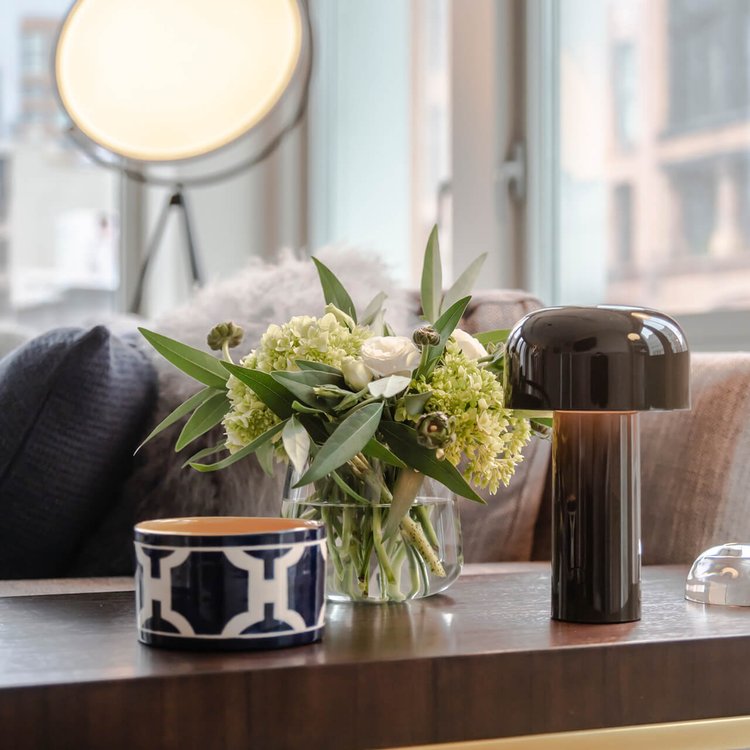 Dark glossy lamp on a wooden table beside a flower bouquet and a patterned bowl 16