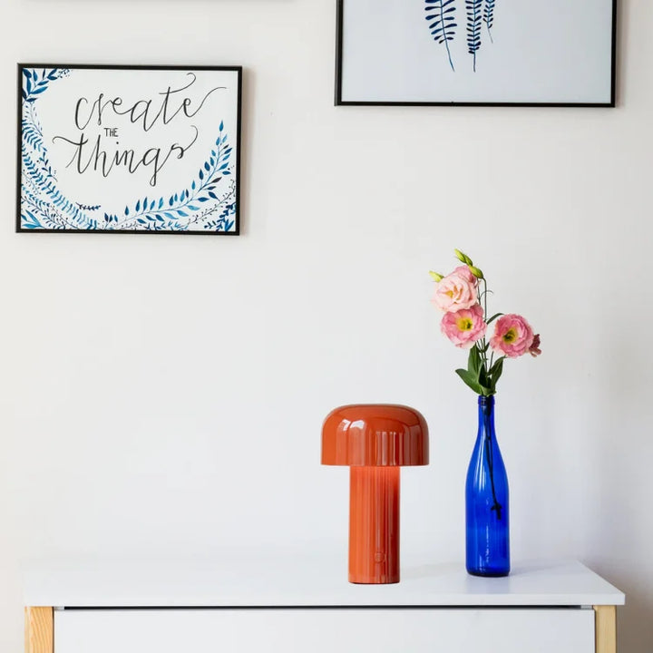 Orange lamp on a white dresser next to a blue vase with pink flowers and framed prints 20