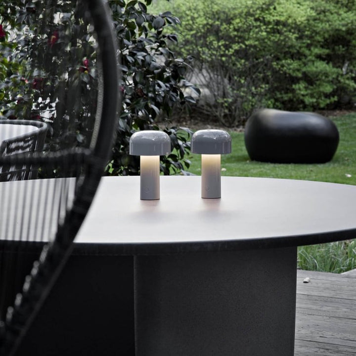 Pair of gray mushroom lamps lit on a round outdoor table with a garden behind 23